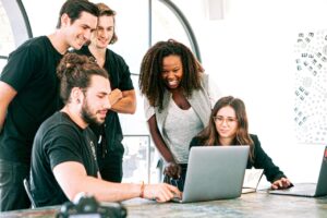 A Group of millennials huddled around a MacBook in an office